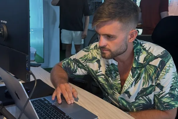 Mateusz Popławski w koszuli w liście palmowe pracuje przy laptopie w coworkingu